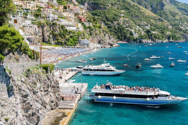 Scenic Amalfi Coast in Italy with colorful cliffside buildings, turquoise water, and boats along the Mediterranean coastline.