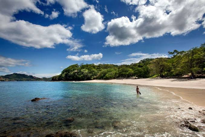 Tropical beach in Costa Rica with turquoise water, golden sand, lush green trees, and a bright blue sky.