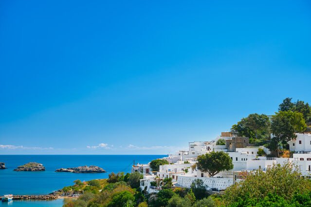 Whitewashed buildings along the coast of Santorini, Greece, overlooking the deep blue Aegean Sea under a clear blue sky.