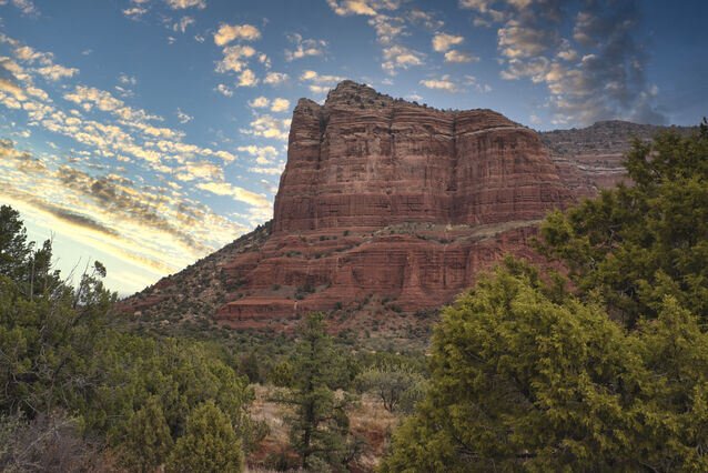 Red sandstone cliffs and desert vegetation in Sedona, Arizona, beneath a partly cloudy sky.