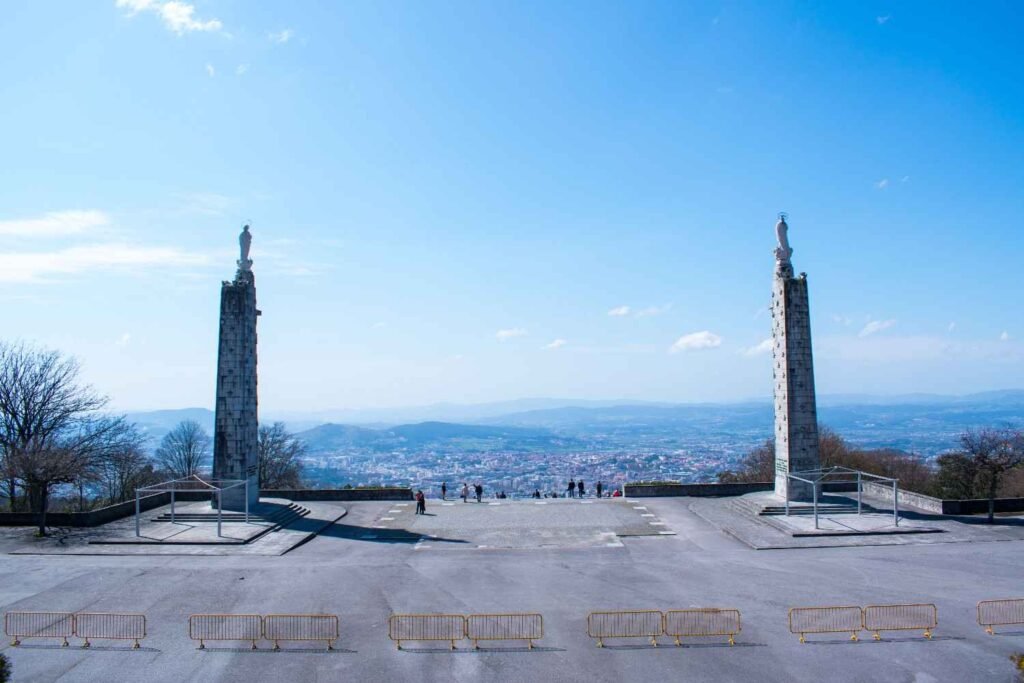 Panoramic view from a hilltop sanctuary in Braga, Portugal, with twin stone towers and a distant cityscape.