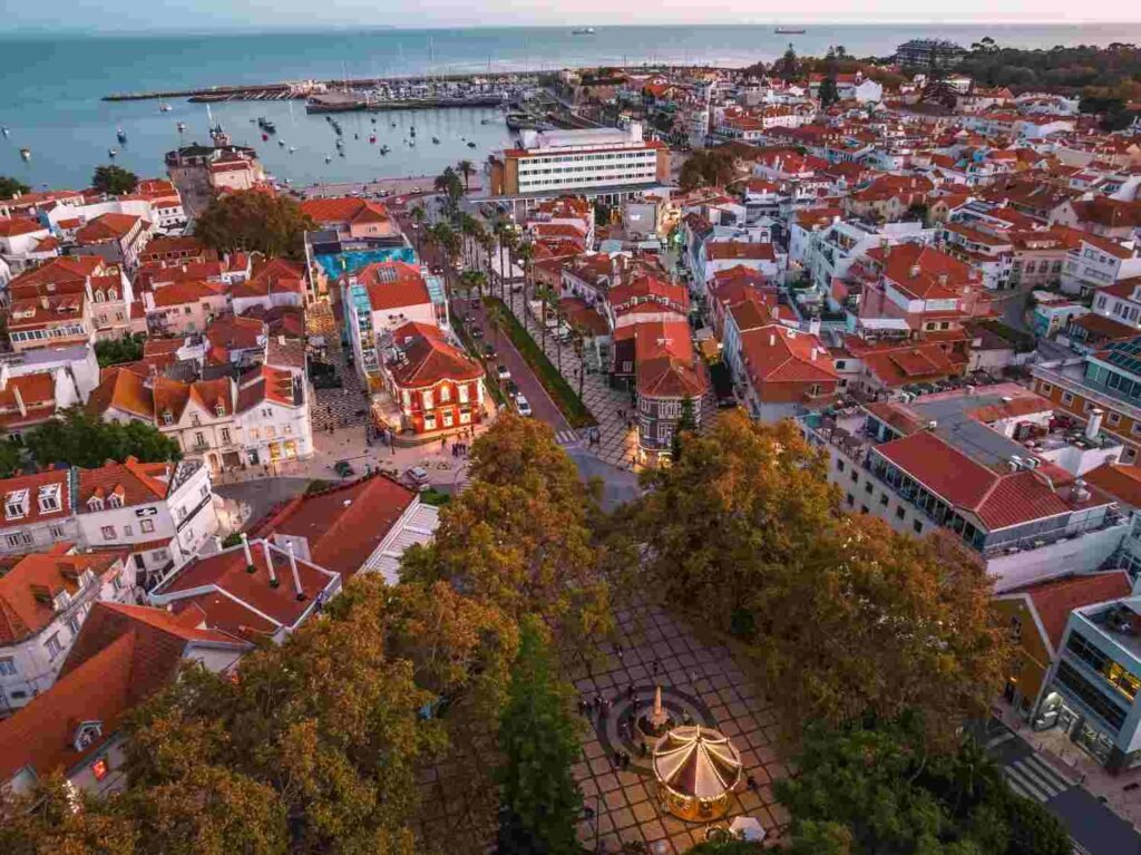 Aerial view of Cascais, Portugal, with red-roofed buildings, a coastal promenade, and the Atlantic Ocean.
