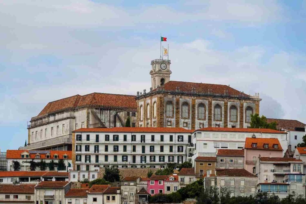 Historic University of Coimbra buildings with red-tiled roofs and a clock tower in Portugal.