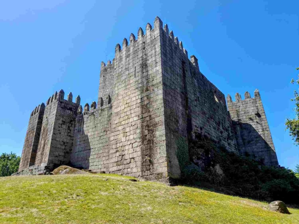 Medieval stone castle with crenellated towers in Guimarães, Portugal, beneath a clear blue sky.