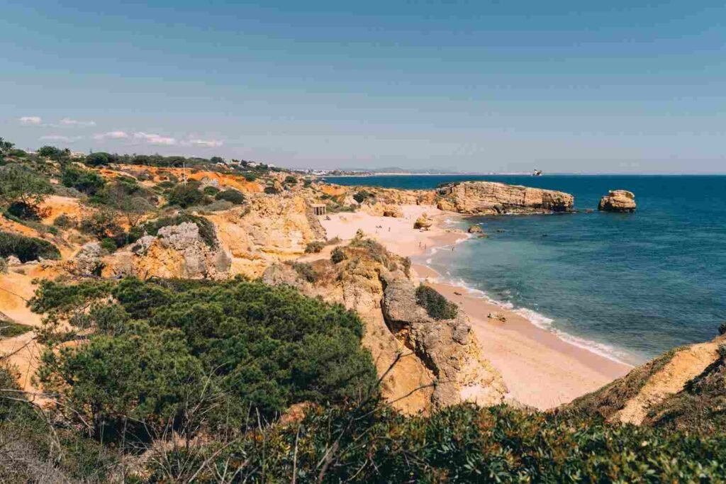 Golden limestone cliffs and a sandy beach beside turquoise water in Portugal’s Algarve region.